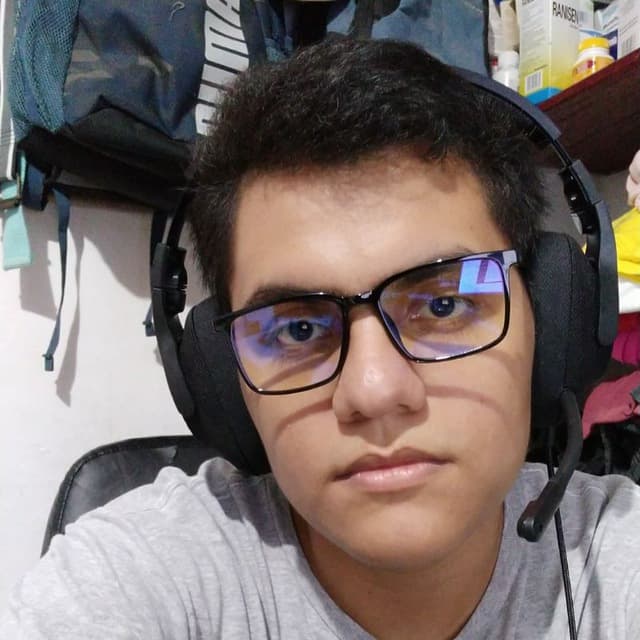 Persona con auriculares y gafas, sentada en una silla en su habitación, mirando a la cámara.