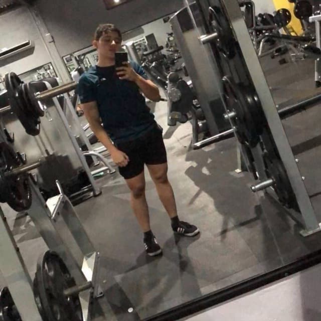 Persona en el gimnasio sosteniendo su teléfono inteligente mientras toma una foto frente a un espejo.