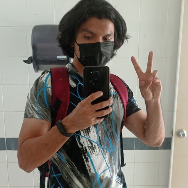 Persona con una máscara facial, tomando una foto frente a un espejo con su teléfono inteligente mientras posa con el signo de la mano de la paz.